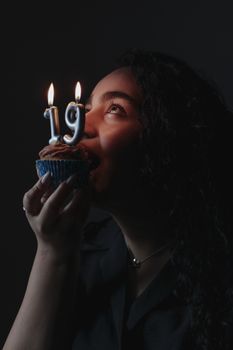 A woman joyfully holds a cupcake with lit candles celebrating her 19th birthday in a dimly lit ambiance.