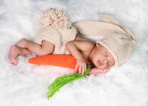 Free Cute baby in a knitted bunny costume sleeping on white fur holding a toy carrot. Stock Photo