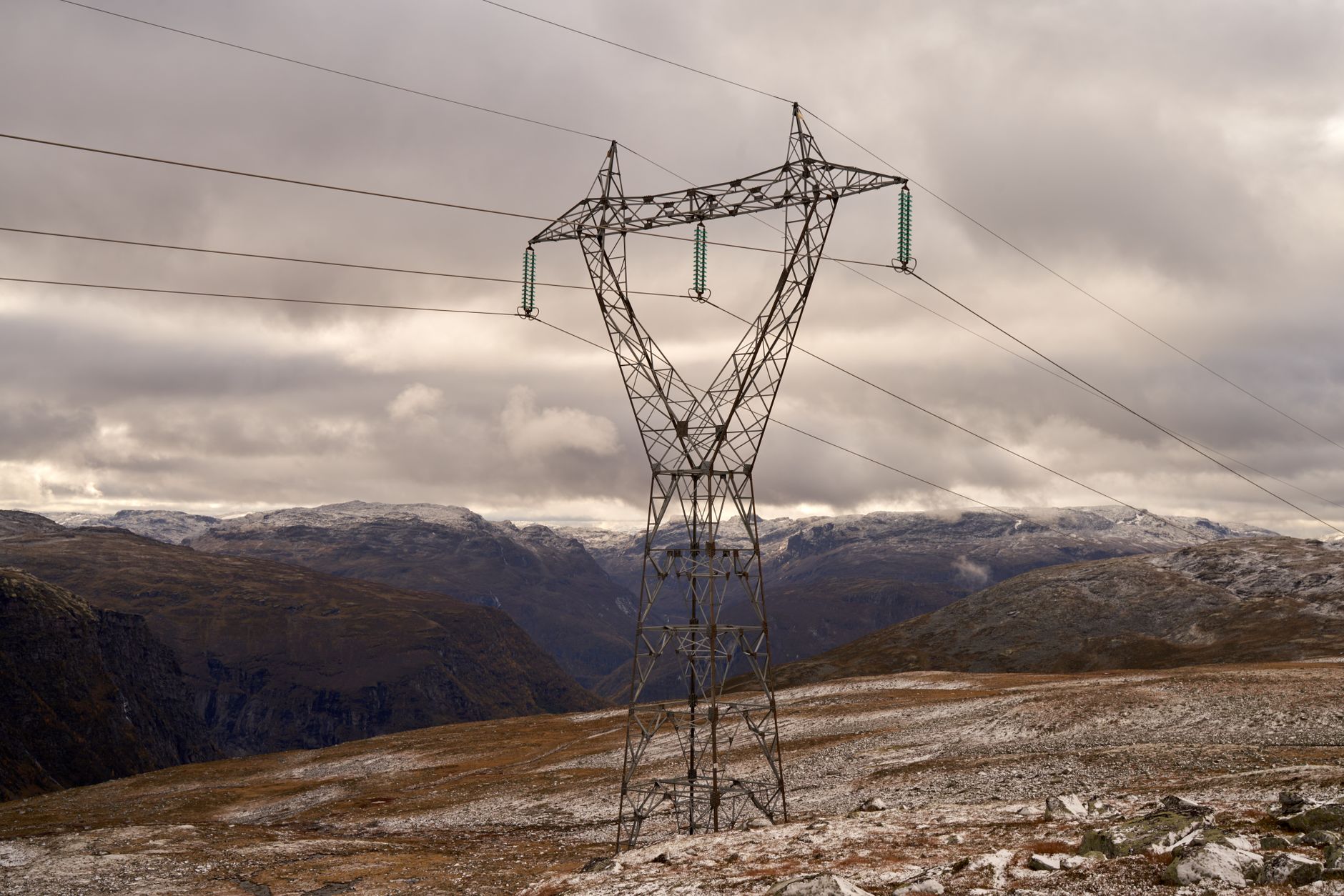 Electricity pylons in Aurlandsvangen, Norway against rugged mountains and cloudy skies.