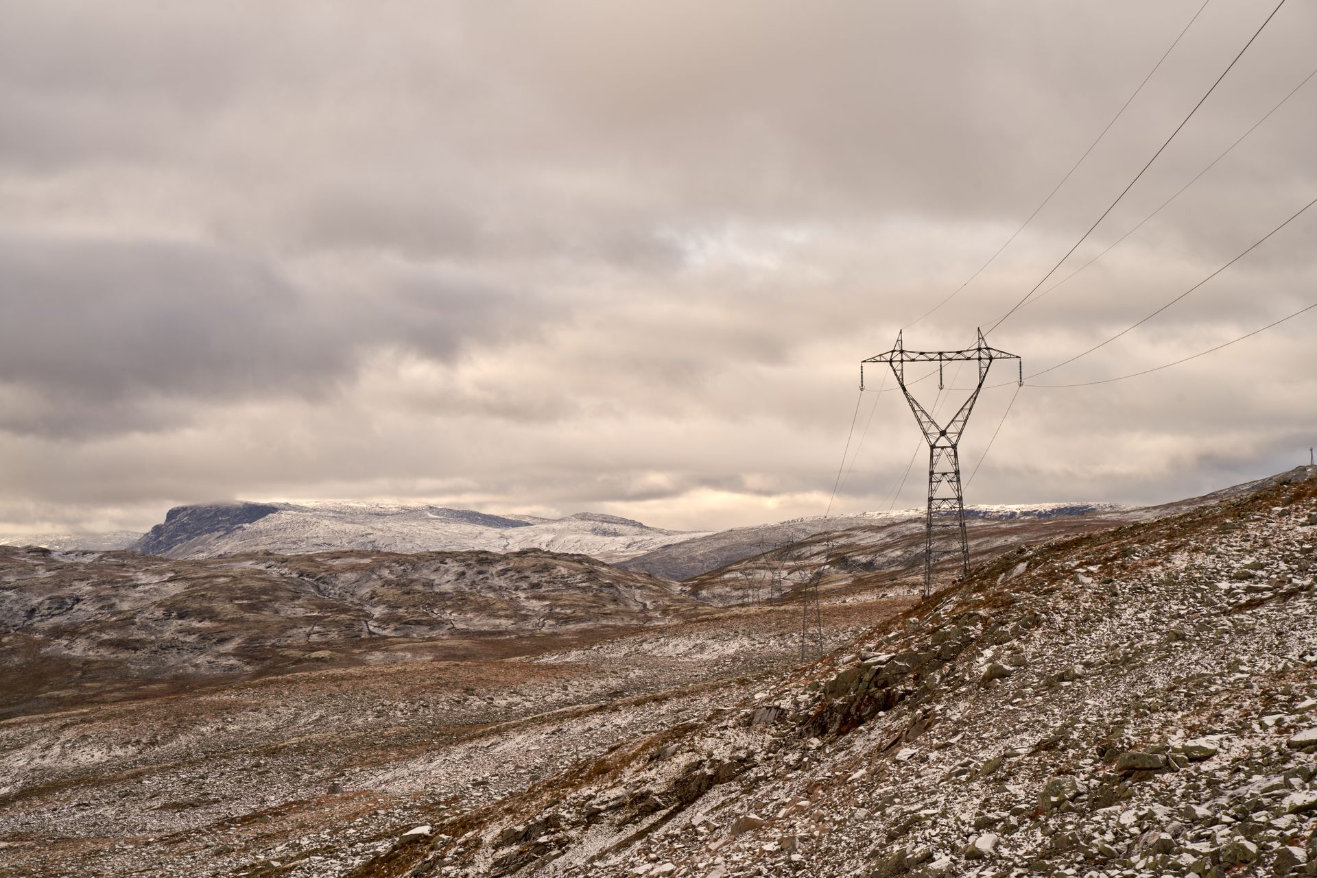 Scenic view of snow-covered Aurland highlands with power lines and a rugged terrain.
