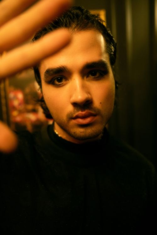 Free A serious man with dark hair and eye makeup poses indoors, creating a moody ambiance. Stock Photo