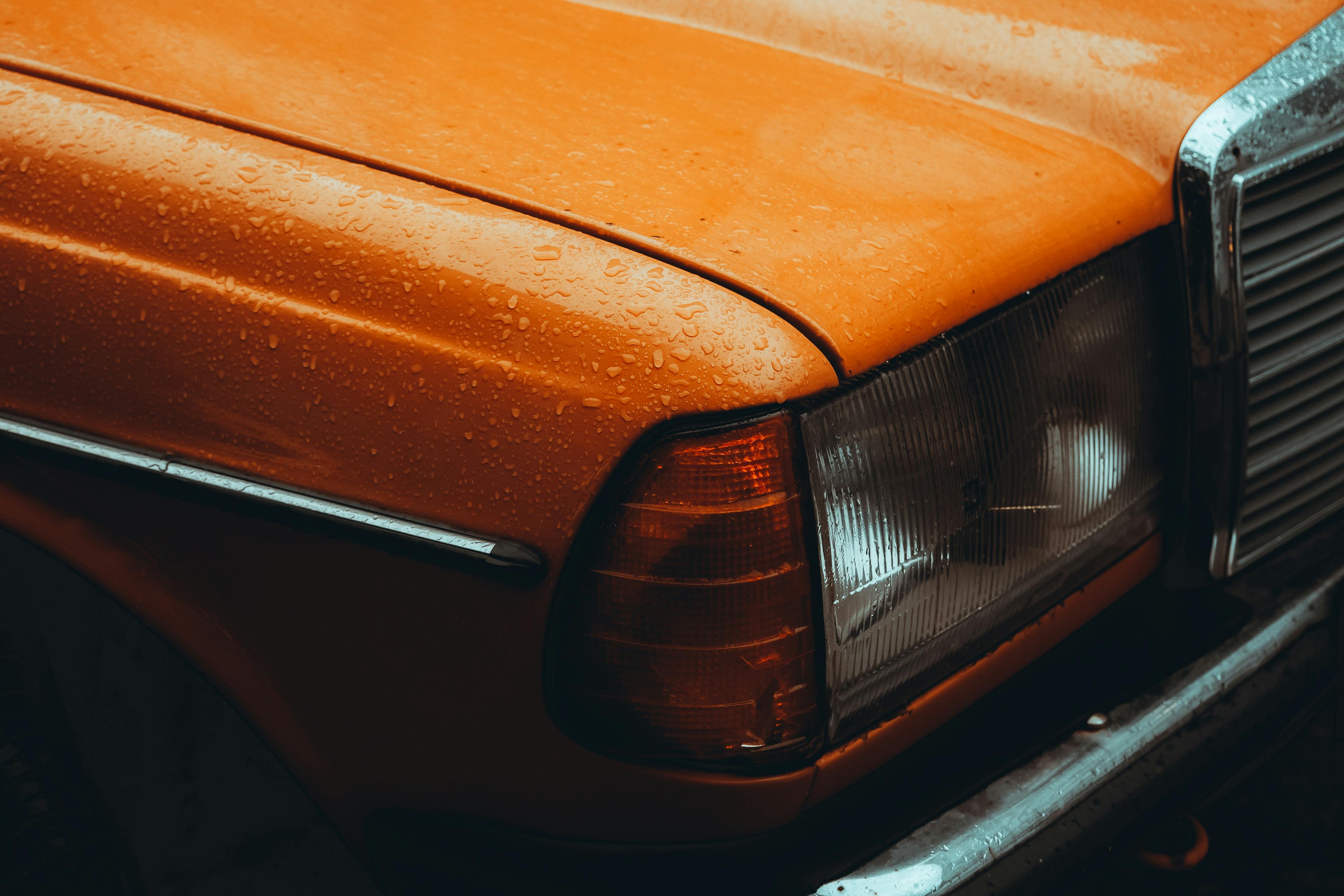 Close-up of a vintage orange Mercedes car with raindrops, showcasing classic automotive design.