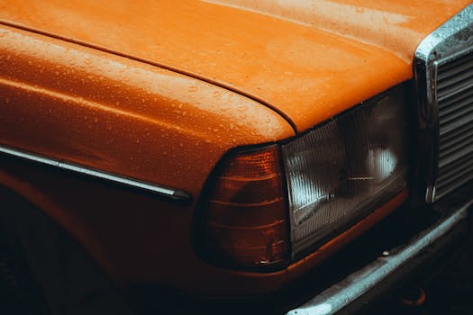 Close-up of a vintage orange Mercedes car with raindrops, showcasing classic automotive design.
