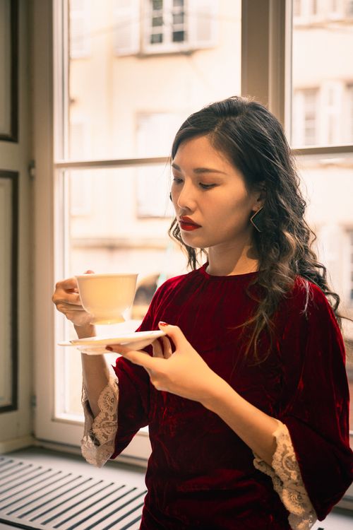 Free Young woman in red dress savoring coffee indoors with a vintage touch. Stock Photo