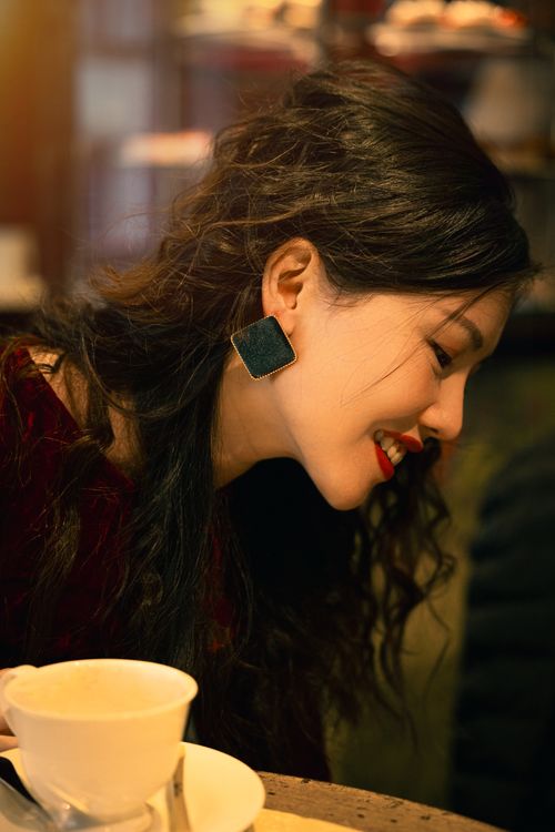 Free Smiling woman with dark hair and earrings enjoying coffee at a cozy indoor cafe. Stock Photo