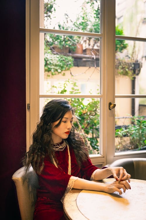 Elegant Woman in a Red Dress Sitting in a Cafe by the Window 