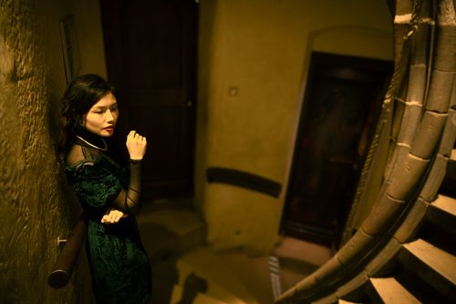 Free An asian woman in a green dress stands by a curved staircase indoors, creating a moody atmosphere. Stock Photo