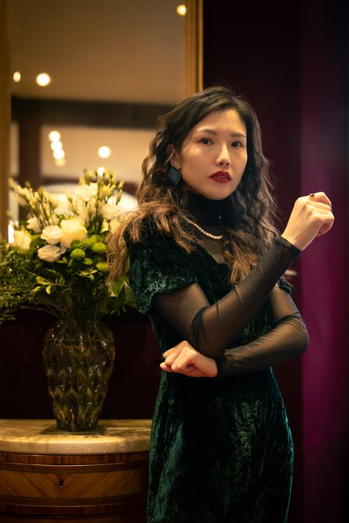 Free Stylish woman in velvet dress beside a mirror with a bouquet, exuding elegance. Stock Photo