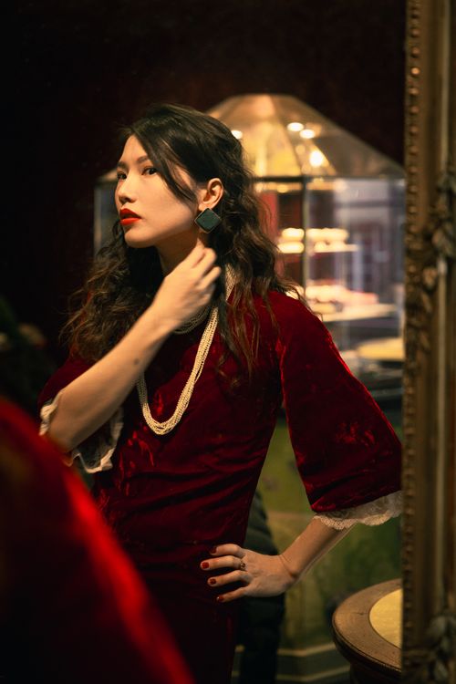 Free Stylish woman in velvet red dress admiring her reflection and applying makeup. Stock Photo