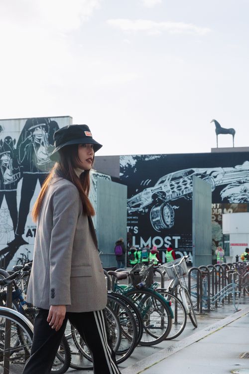 Free Stylish woman walking in city street, surrounded by bicycles and urban art, wearing a trendy hat. Stock Photo