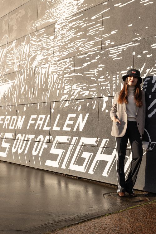 Free A fashionable woman wearing a hat poses by a graffiti wall in an urban setting. Stock Photo