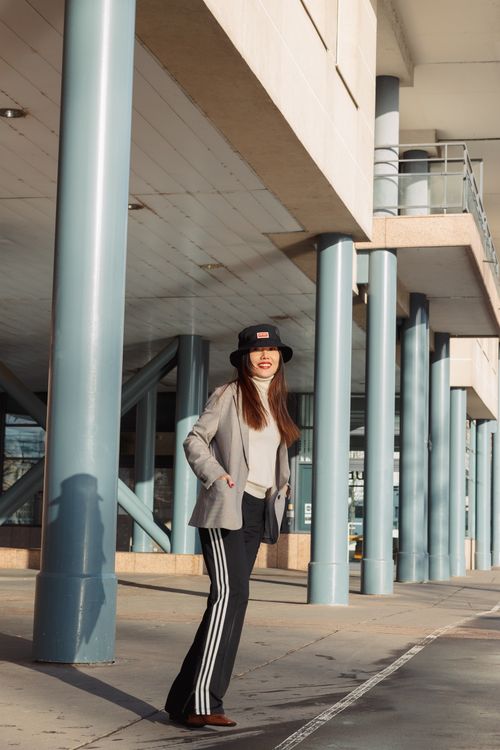 Free A stylish young woman poses in an urban setting wearing a hat and suit jacket. Stock Photo