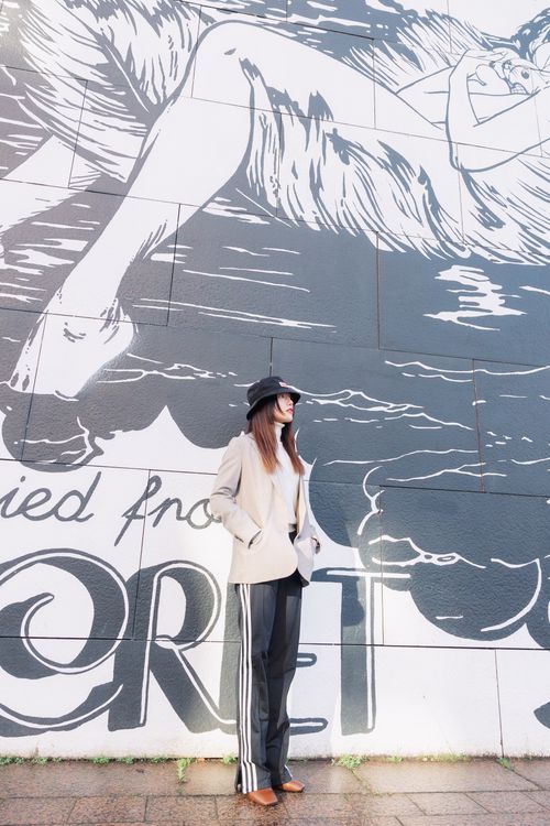 Free Young woman in fashionable attire standing by a large mural outdoors. Stock Photo