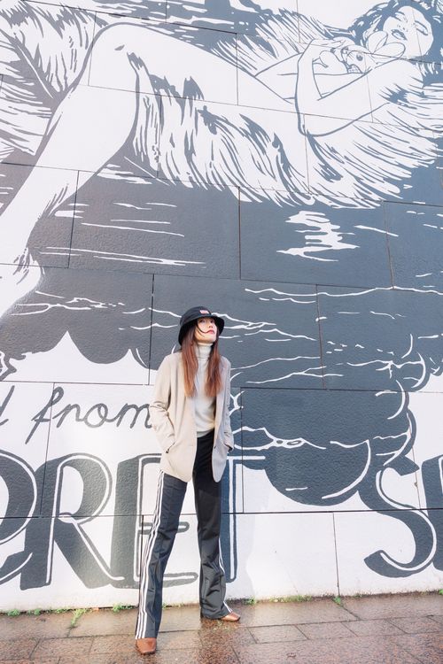 Free Fashionable woman in stylish outfit poses by an urban mural wall. Stock Photo
