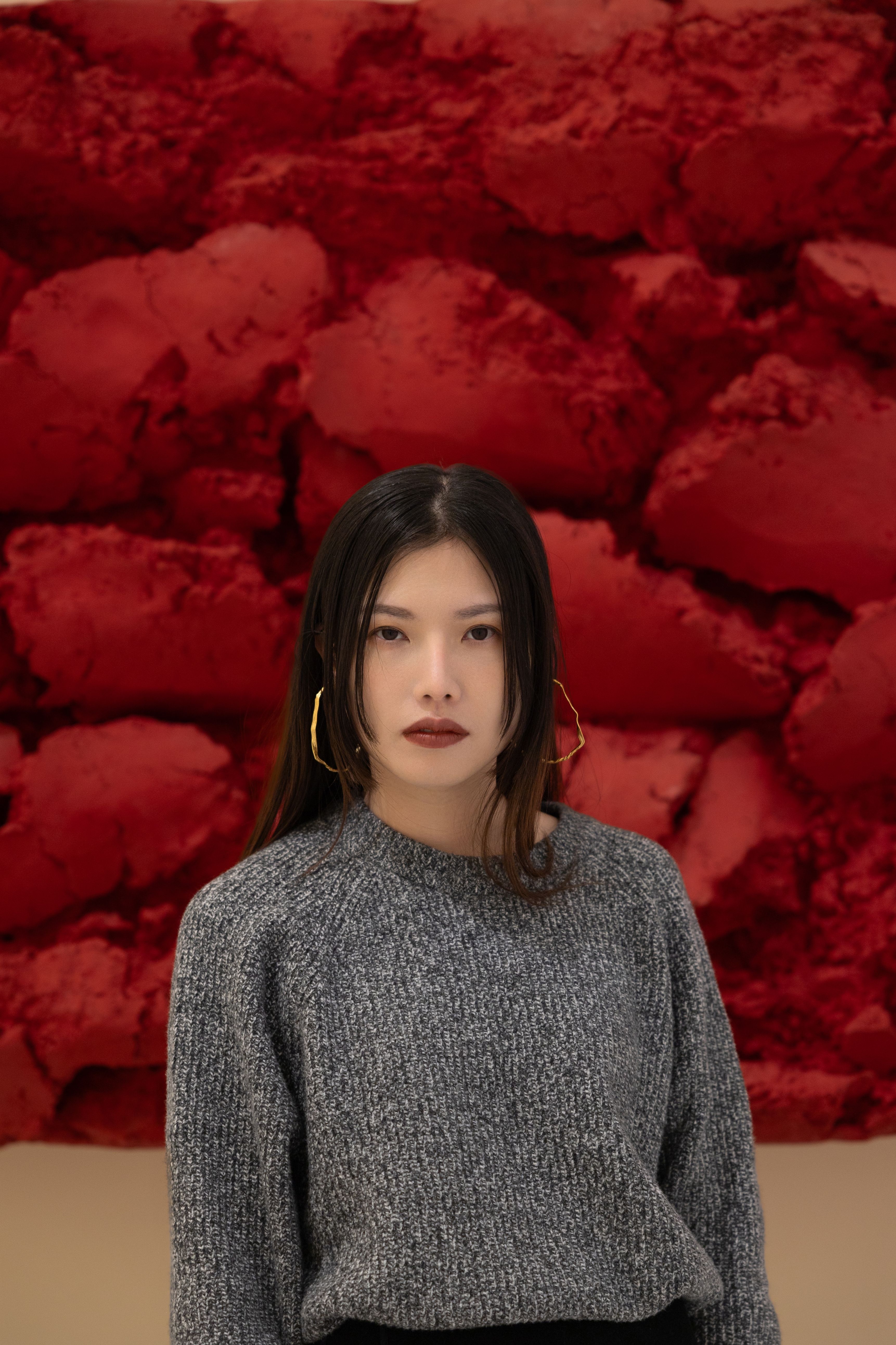 Portrait of a woman in front of a bright red textured background, emphasizing art and style.