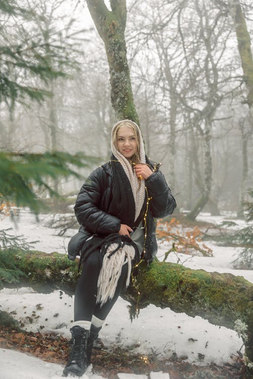 A Woman in Warm Clothing Sitting on a Tree Log in a Forest in Winter 