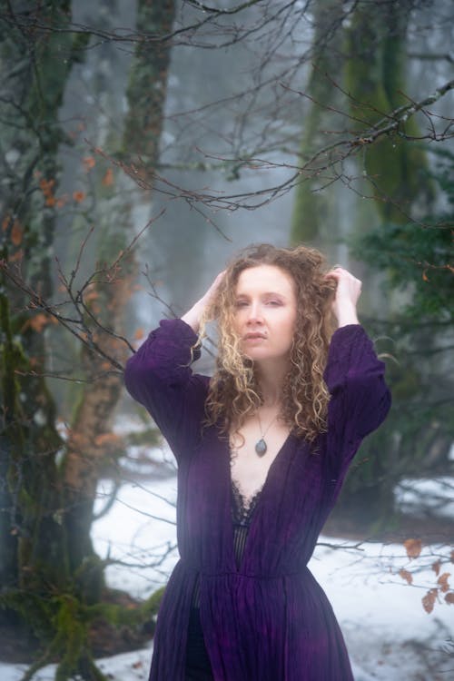 Young Woman Wearing a Purple Dress Posing in a Winter Forest