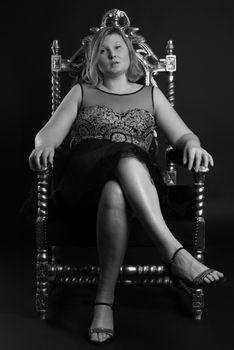 Black and white portrait of an elegant woman seated on an ornate throne, exuding elegance and confidence.