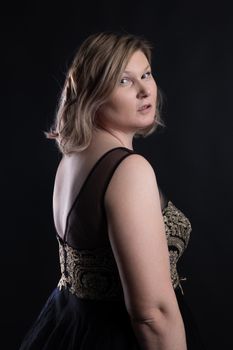 A stylish and elegant woman posing in a glamourous black and gold dress against a dark studio background.