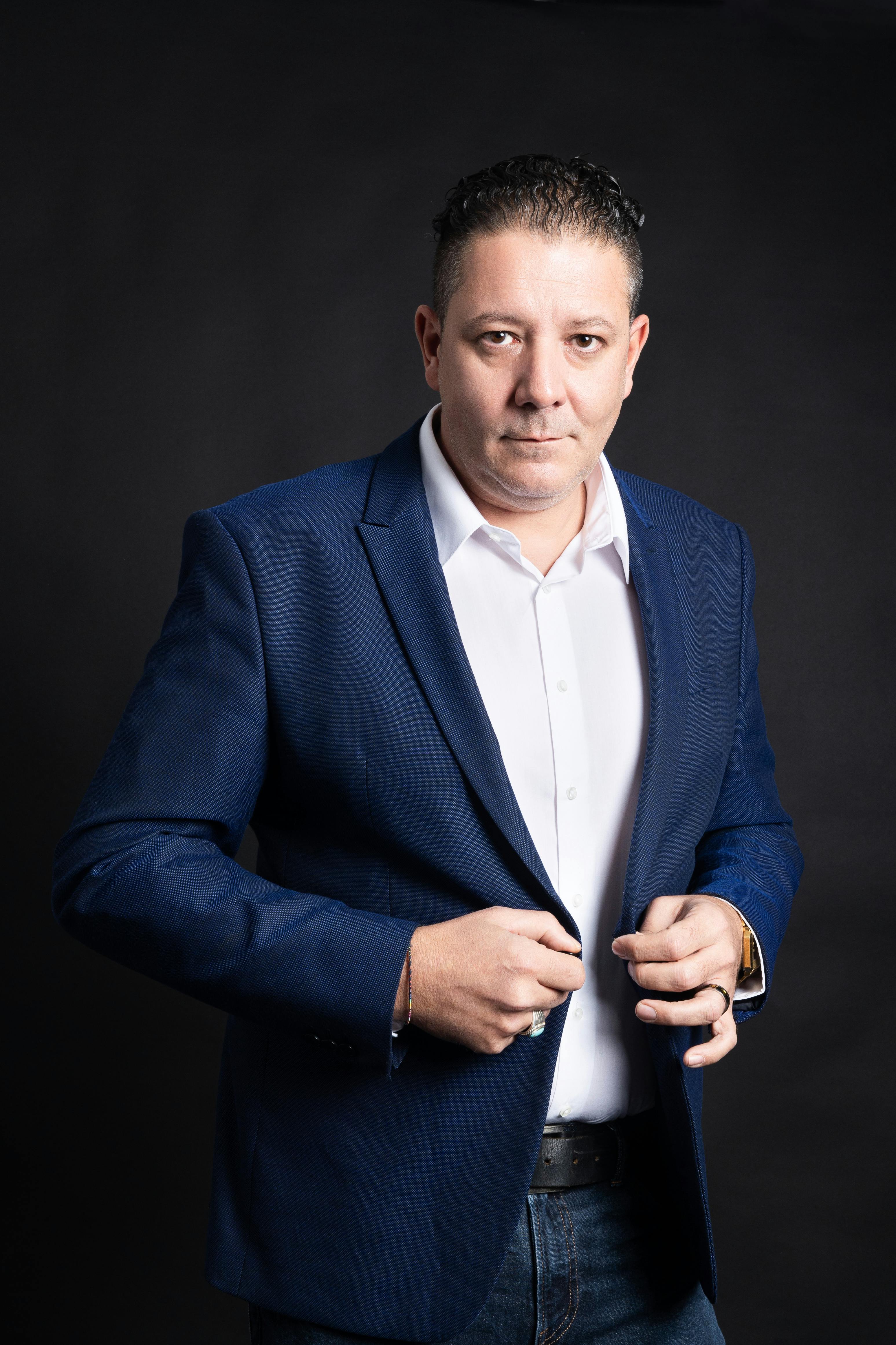Professional portrait of a businessman in a blue suit jacket against a dark background.