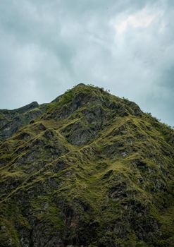 Dramatic view of a lush green mountain peak beneath a cloudy sky, capturing nature's beauty.