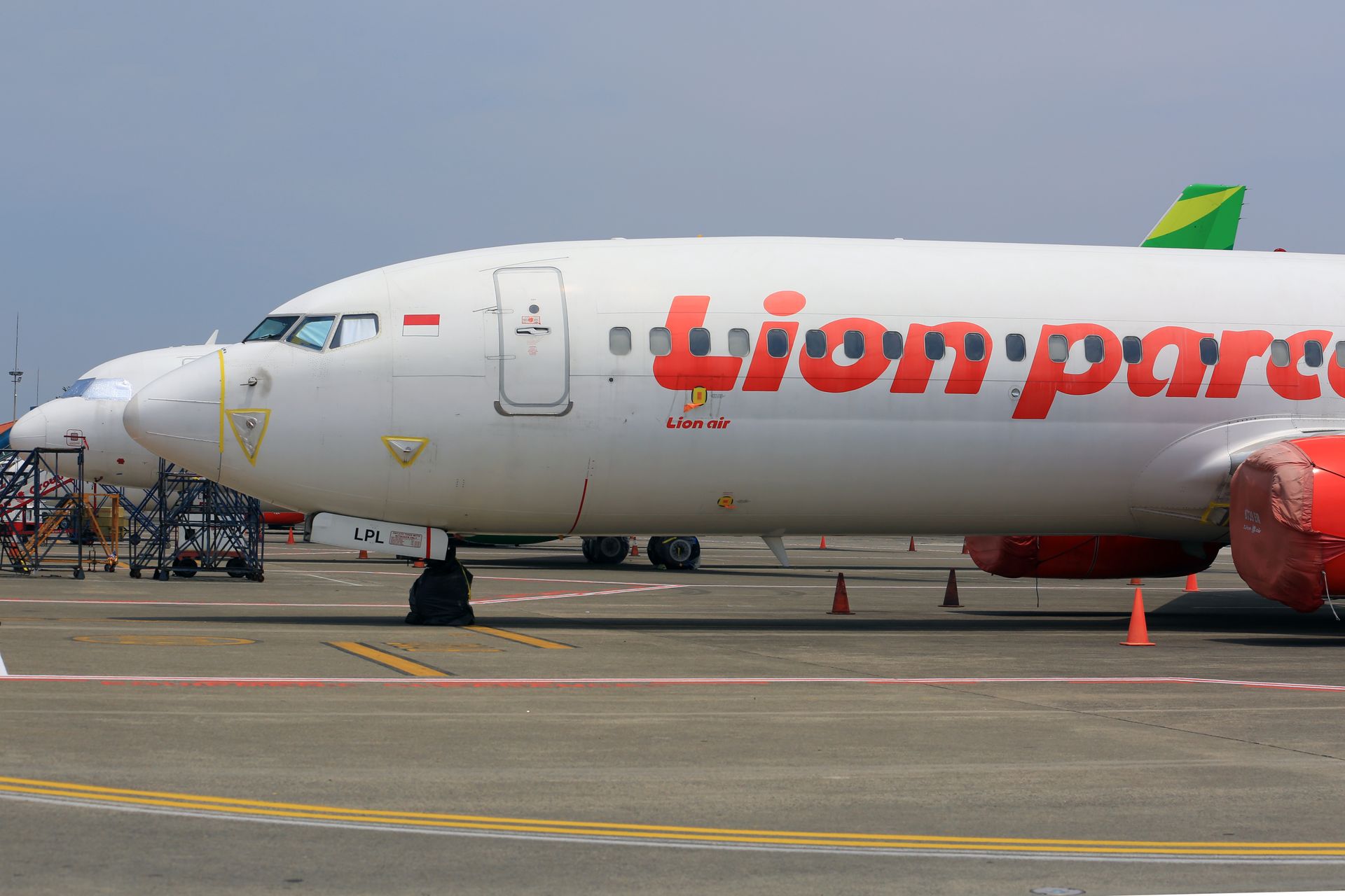 Lion Air airplane parked on a sunny airport tarmac with equipment around.