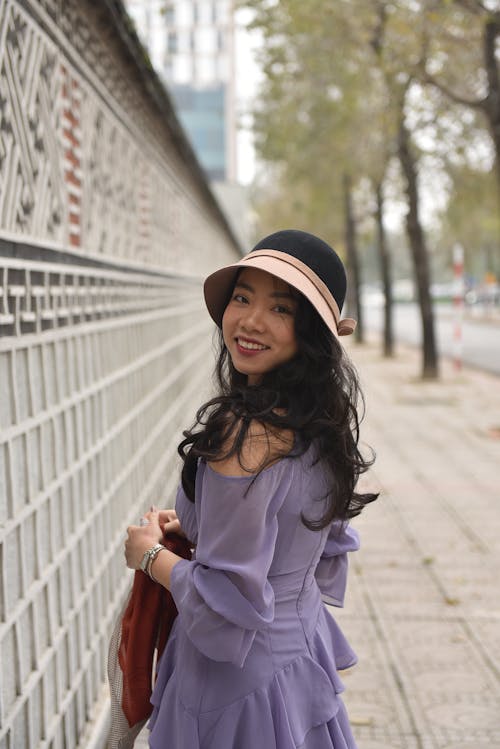 A woman in a purple dress and hat standing on a sidewalk