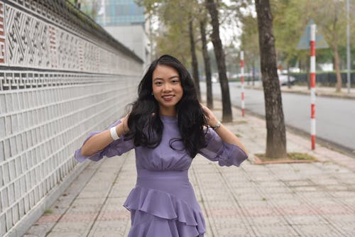 Young Woman in a Dress Standing on a Sidewalk in City and Smiling 