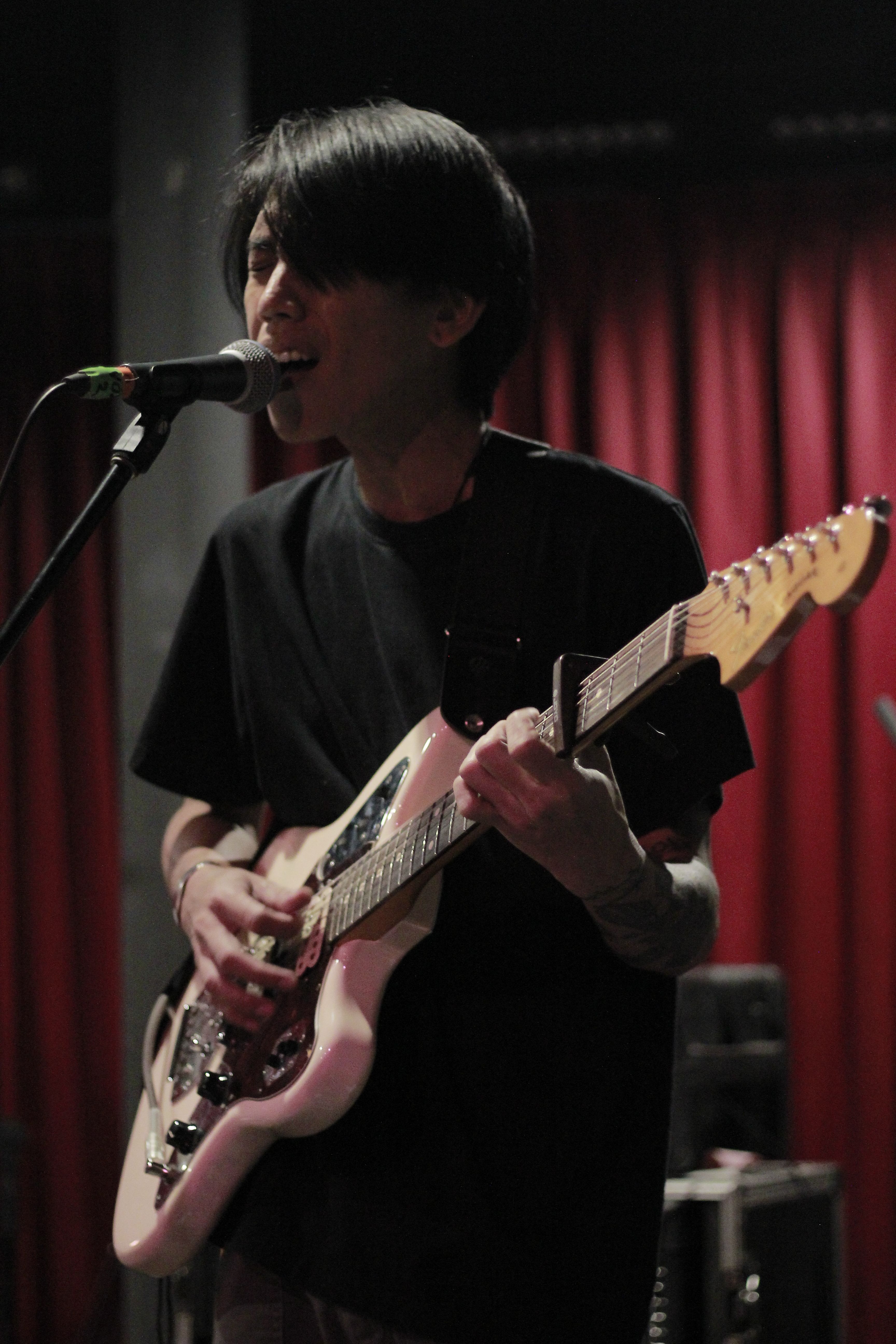 Musician passionately playing electric guitar on stage in a dimly lit club setting.