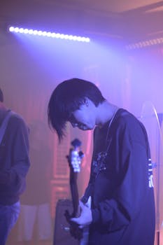 A guitarist plays passionately on stage amid purple lighting at a live concert.