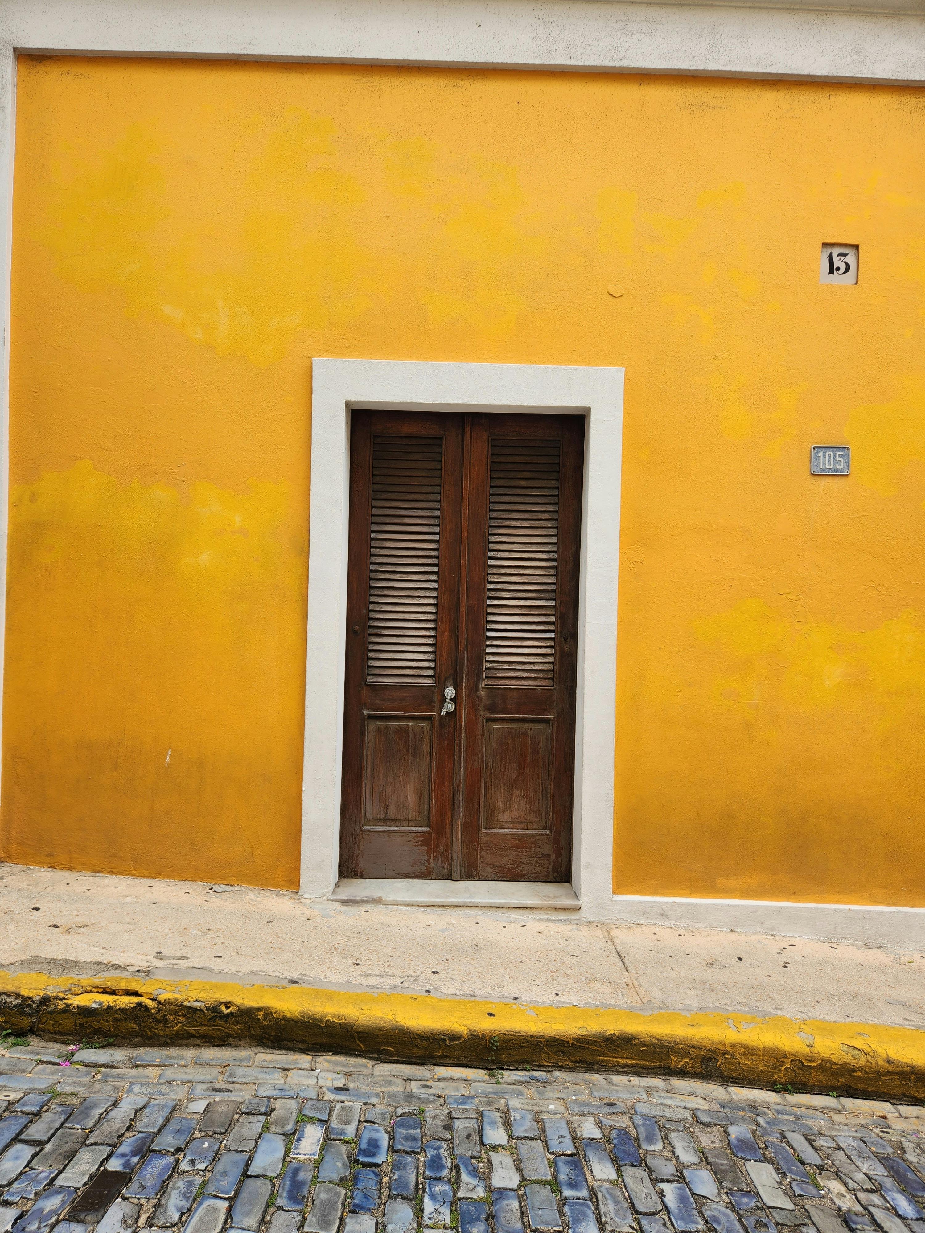 Vibrant yellow building facade with shuttered wooden door in historic San Juan, Puerto Rico.