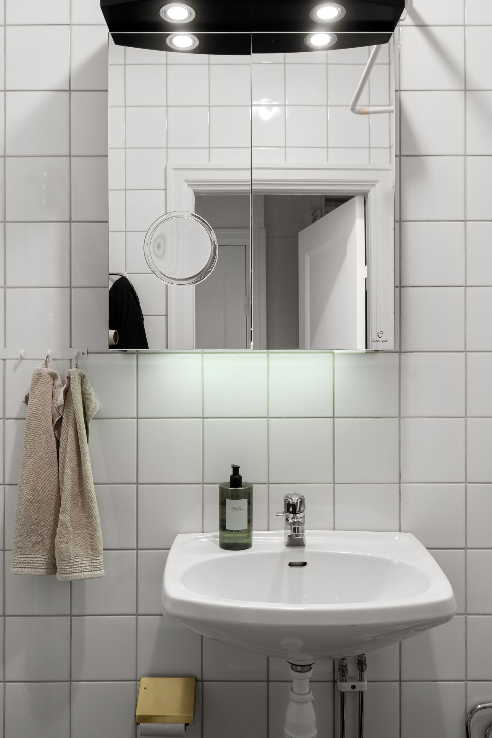 White-tiled bathroom with a simple wall-mounted sink and mirror; style reference, not a documented renovation before and after.