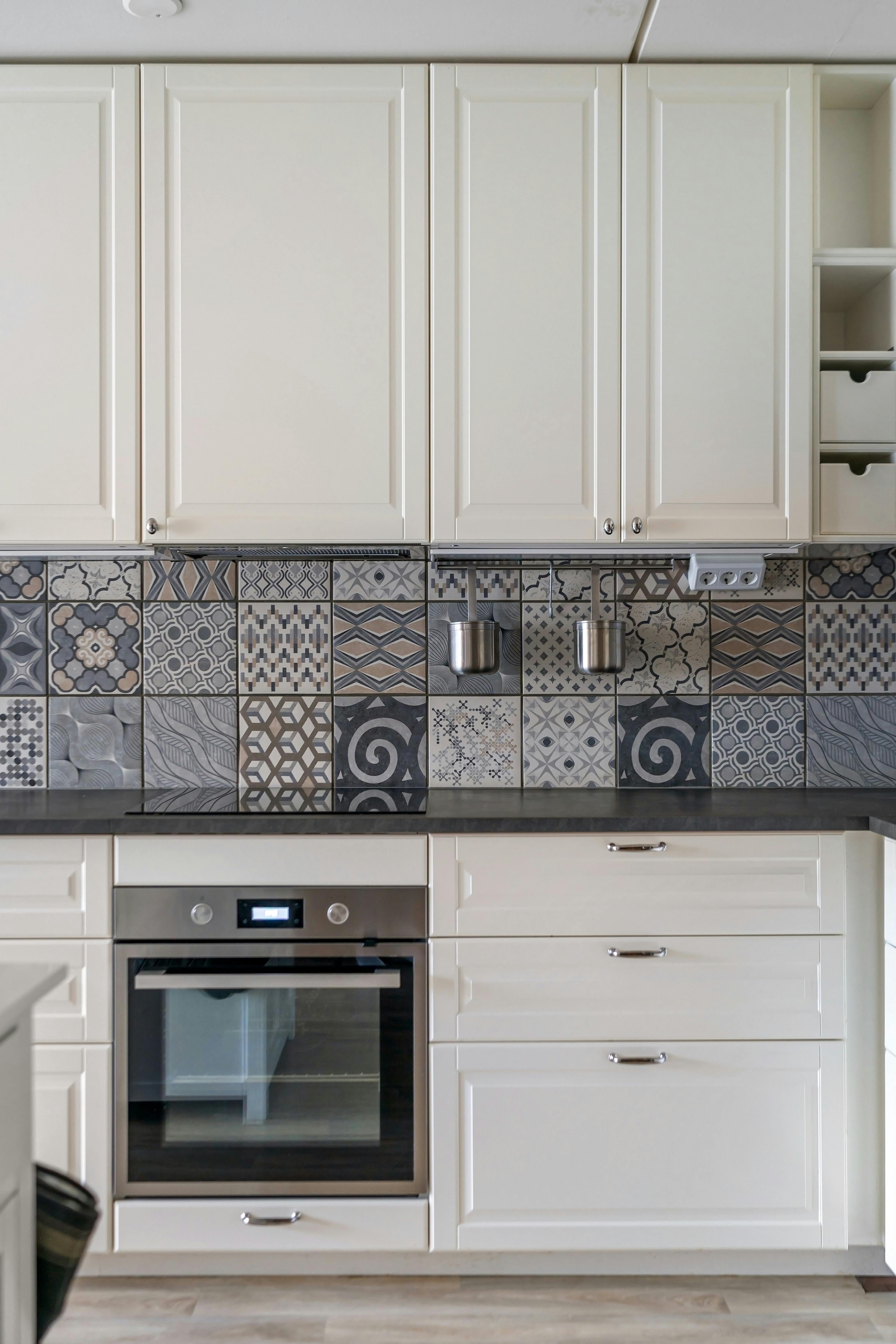Elegant kitchen design featuring white cabinets and a patterned mosaic tile backsplash.
