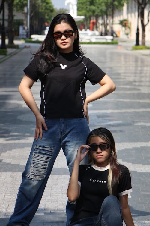 Women in Black T-shirts Standing and Sitting on Pavement