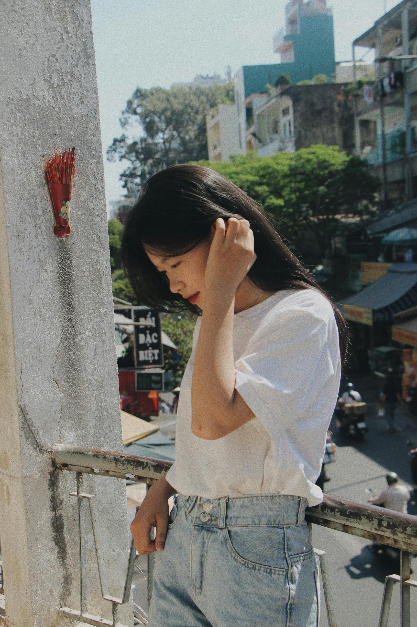 Asian woman in the city, enjoying a moment of reflection on a sunlit balcony.