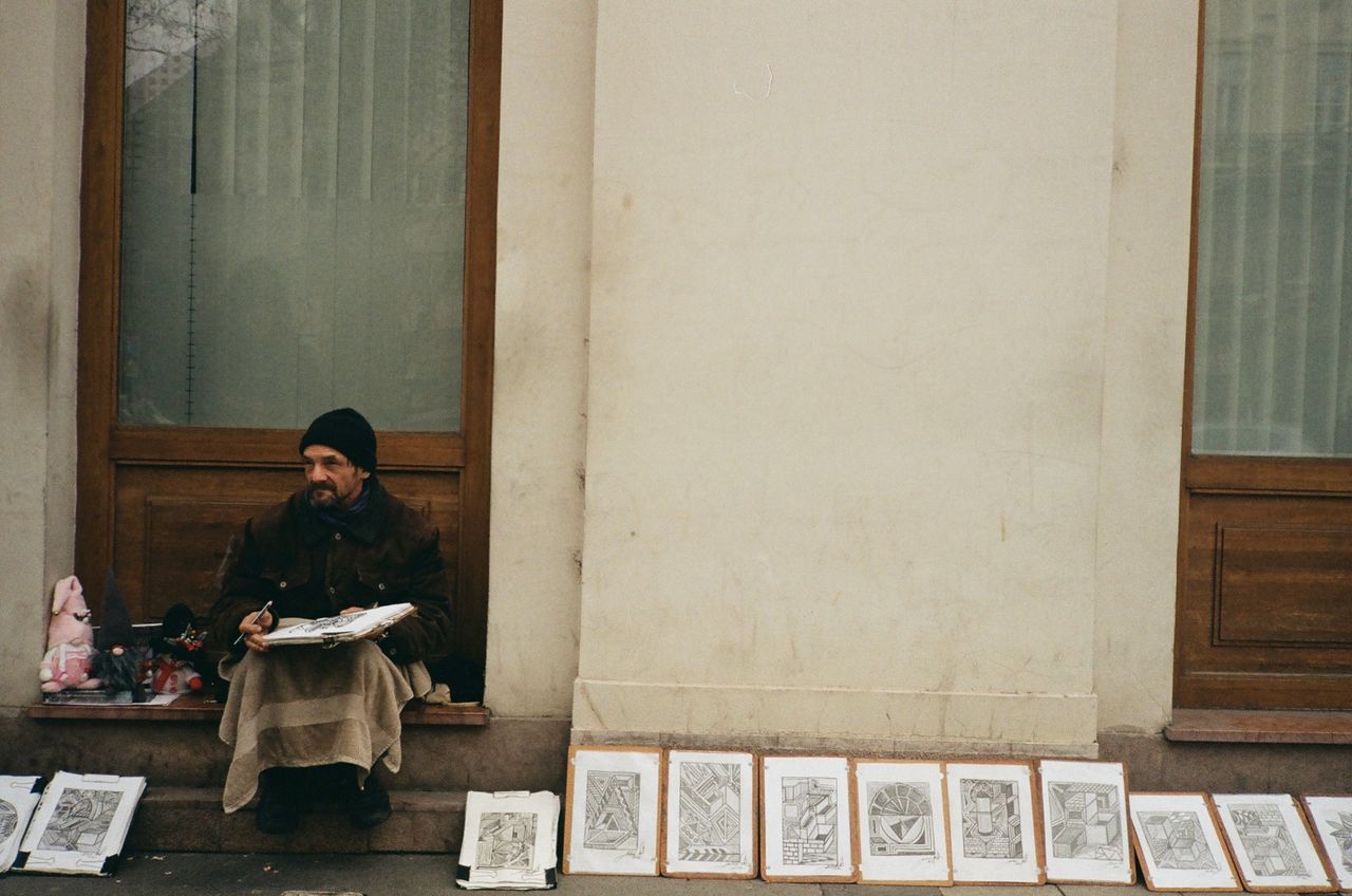 a street artist in budapest sits by the sidewalk with his artworks on