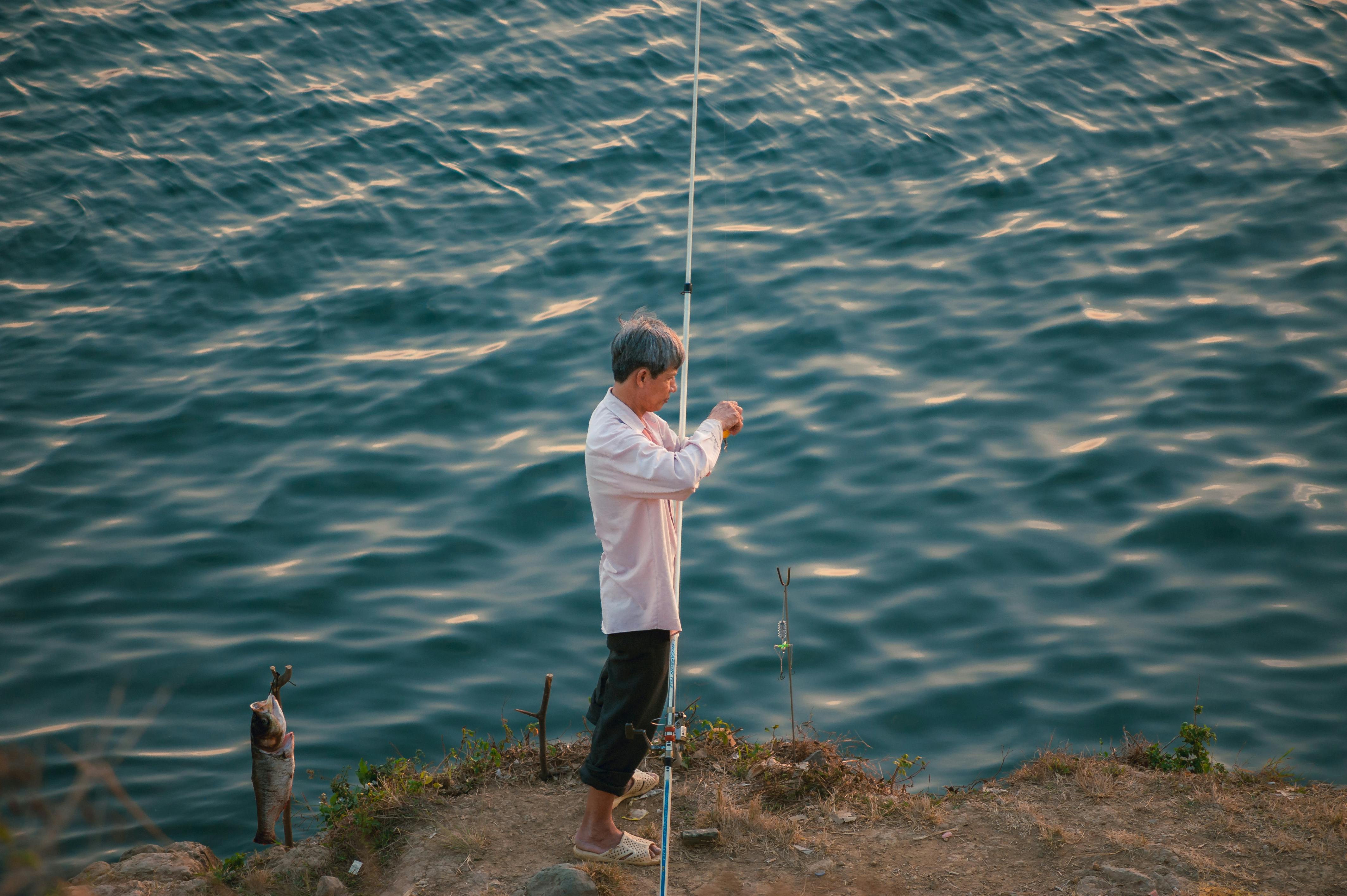 A senior man fishing on a rocky cliffside by the sea, enjoying a peaceful outdoor moment.