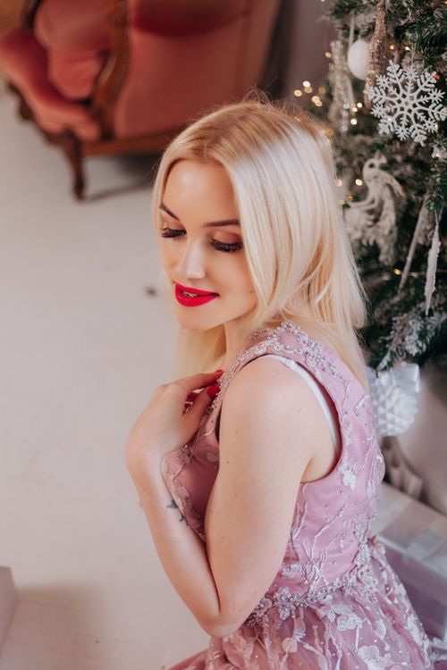 Free Elegant blonde woman with red lips poses near a decorated Christmas tree indoors, exuding a festive and stylish charm. Stock Photo