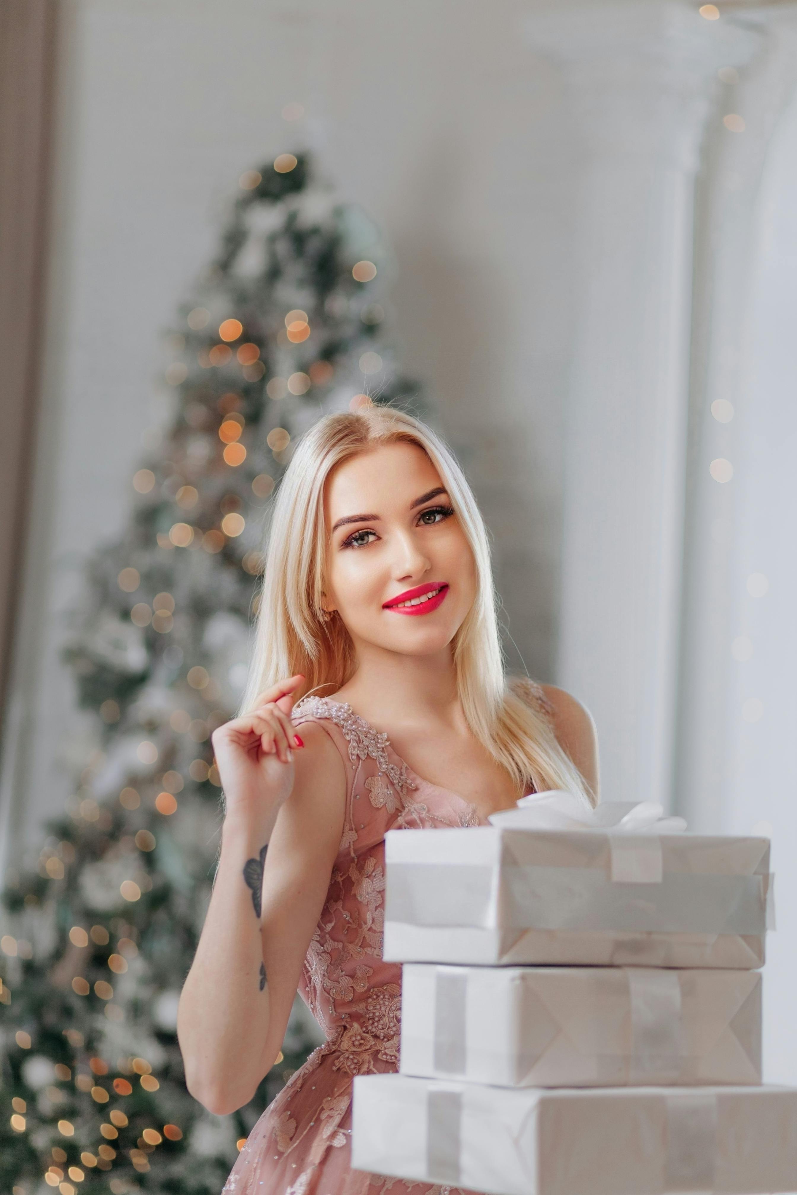 Blonde woman in pink dress smiling with Christmas gifts indoors