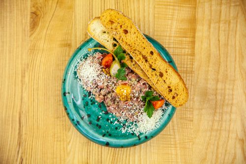 Free Delicious beef tartare plated with cheese, tomato, and crispy bread on a turquoise dish. Stock Photo