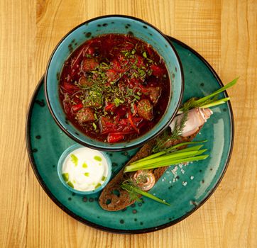 Top view of a traditional borscht served with garnish and cream on a rustic wooden table.