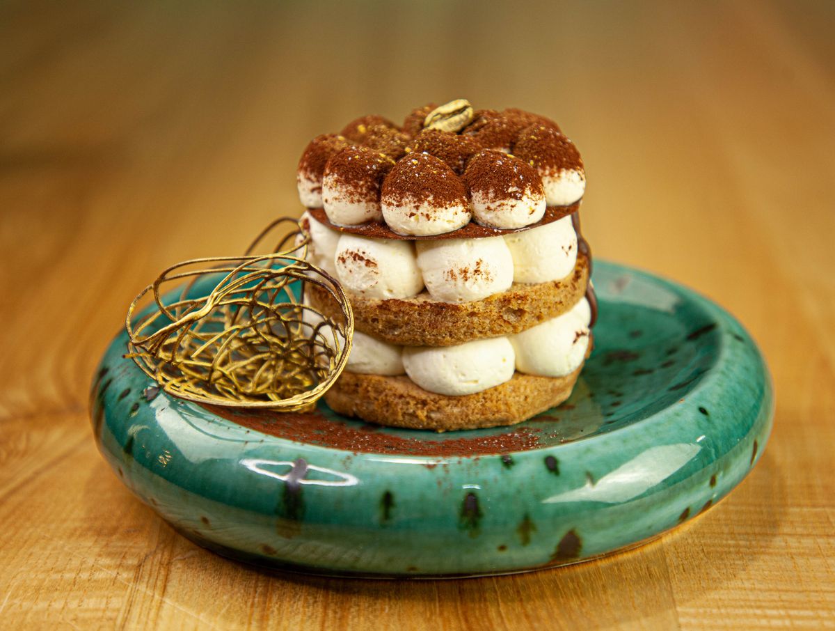 Tiramisu tower of sponge rounds and piped mascarpone dollops dusted with cocoa on green plate