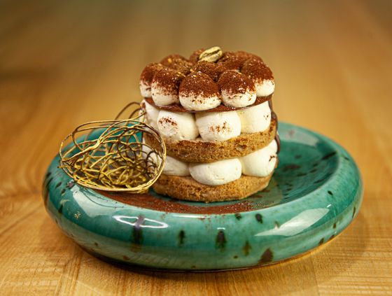 Tiramisu tower of sponge rounds and piped mascarpone dollops dusted with cocoa on green plate