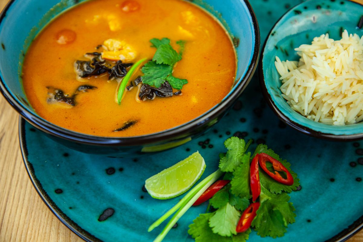 Orange coconut red curry soup with shrimp, wood ear mushrooms and cilantro beside jasmine rice