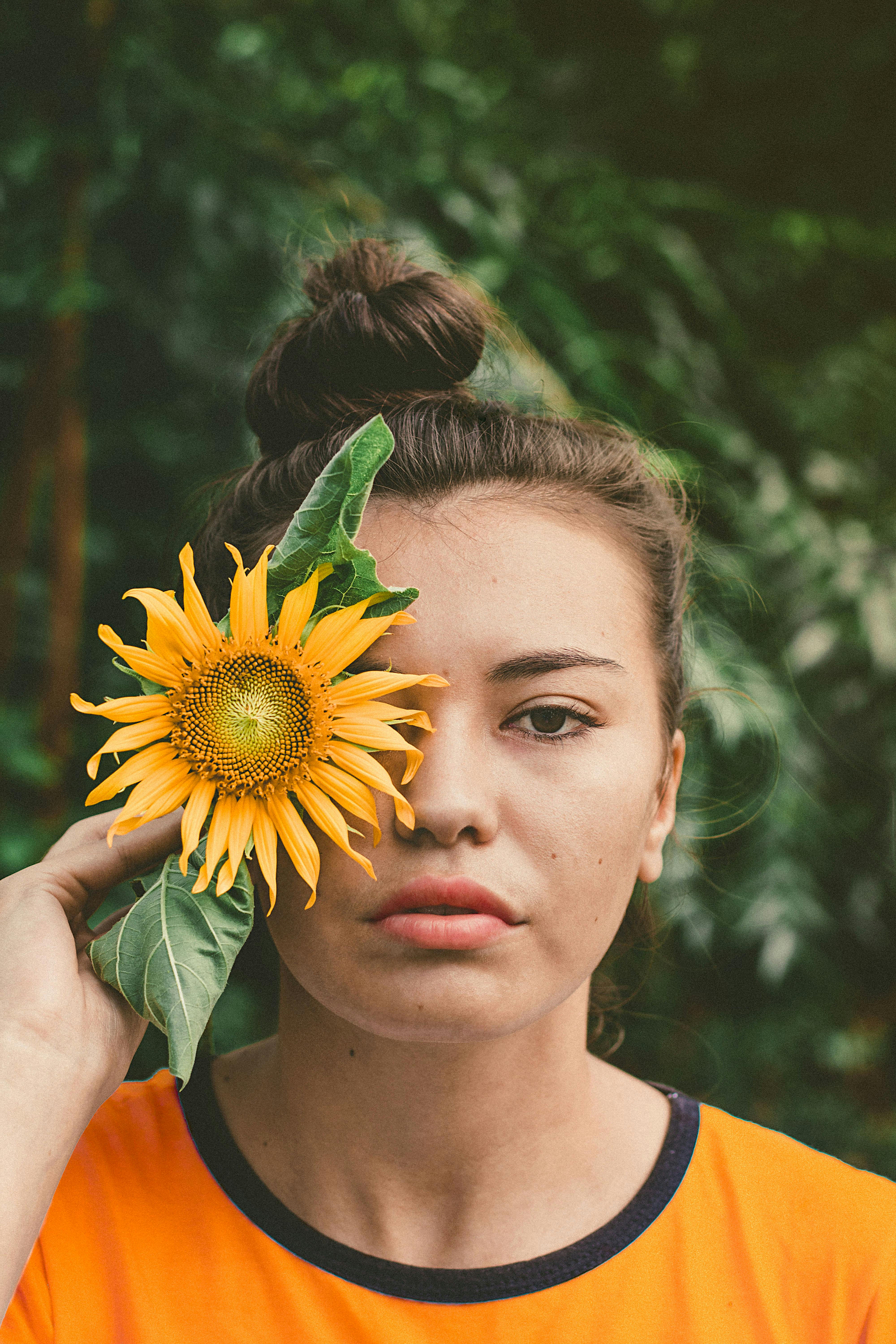 Young woman holding sunflower to her face outdoors, exuding a playful and natural vibe.