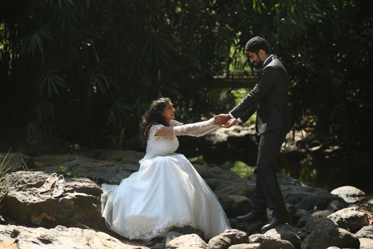 Joyful newlyweds holding hands on a rocky hillside in a serene park setting.