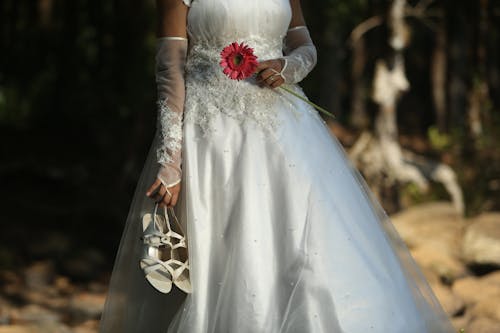 Bride in Wedding Dress Holding Flower and Shoes