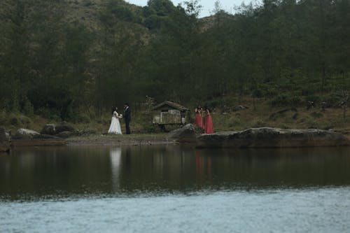 Newlyweds and Women in Dresses Standing by Lake