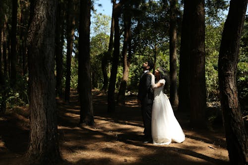 Cute Bride in Wedding Dress Embracing Groom in Suit in Forest