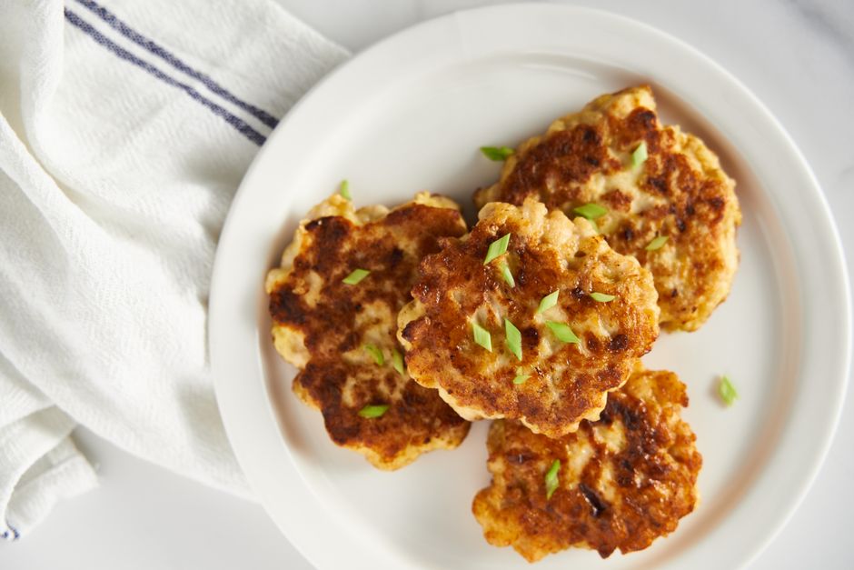Golden-brown chicken apple sausage patties stacked on a plate with a skillet in the background.